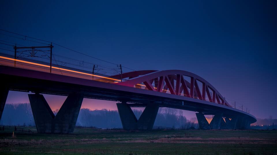 A bridge with red trusses and a train passing underneath.