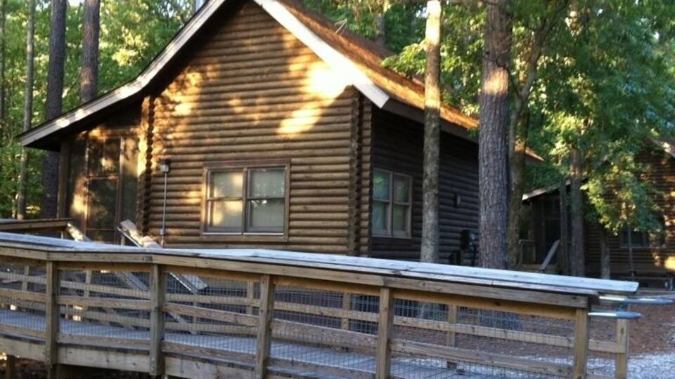 A wooden cabin with a metal roof, surrounded by tall trees and a wooden deck.