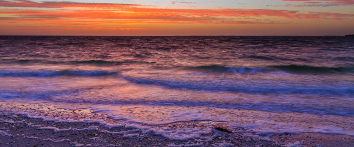 A sunset over the ocean with waves crashing onto the shore.