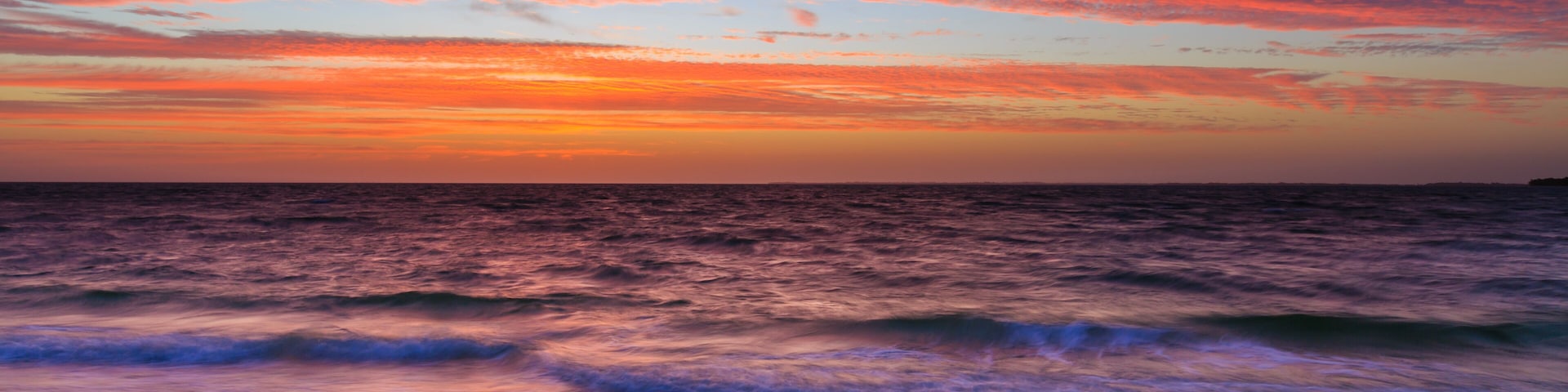 A sunset over the ocean with waves crashing onto the shore.
