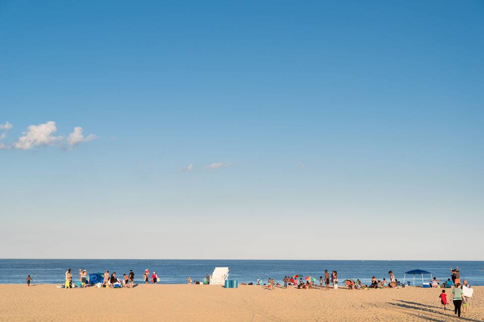 Ein sandiger Strand mit Menschen, Sonnenschirmen und einem blauen Zelt.
