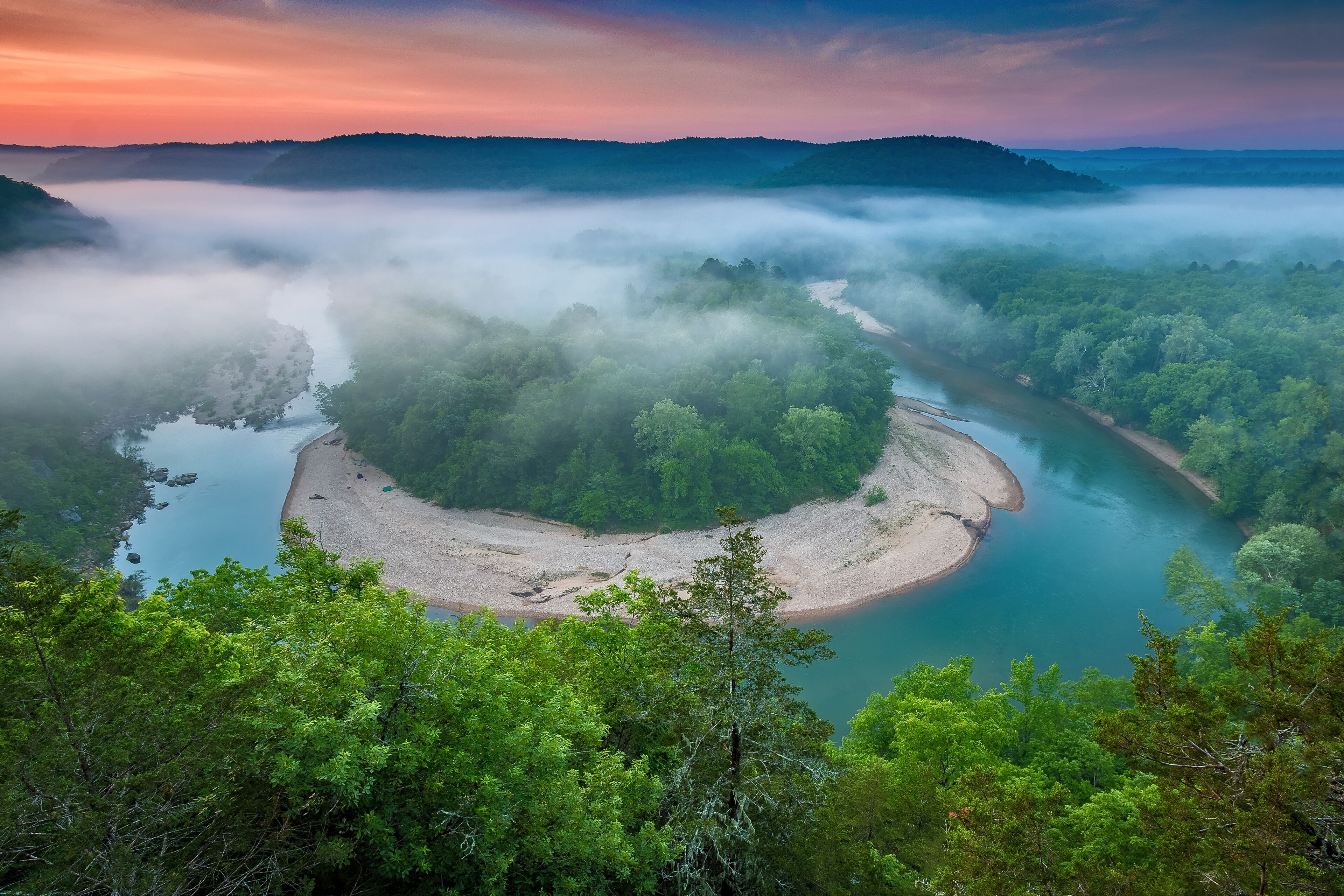 A river winding through a forested valley with a sandy island in the center.
