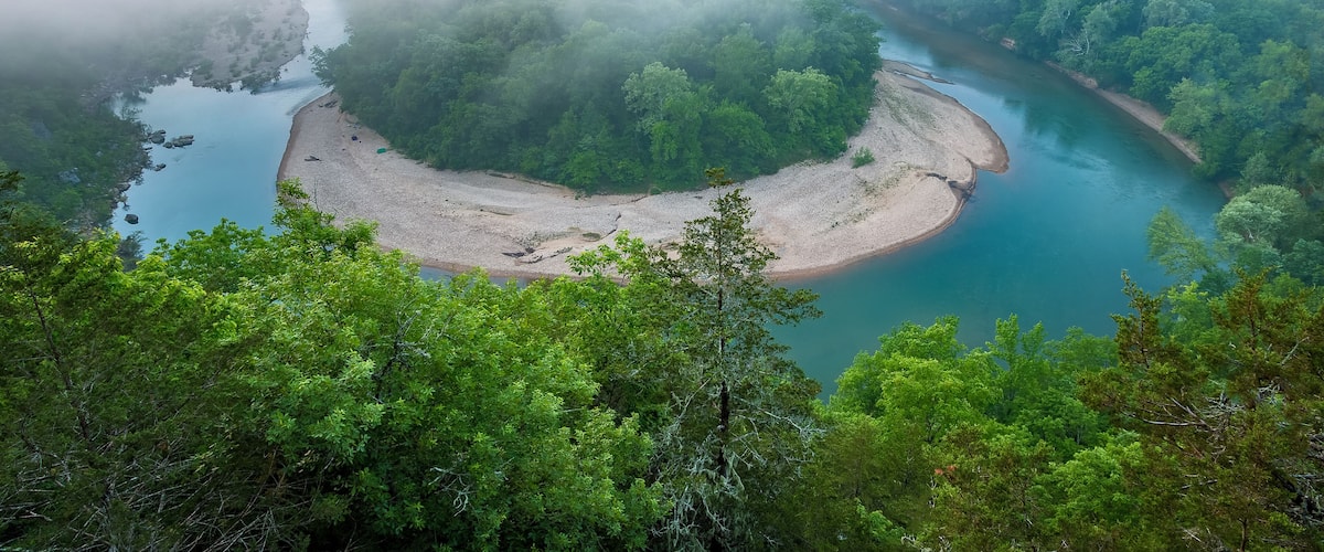 A river winding through a forested valley with a sandy island in the center.