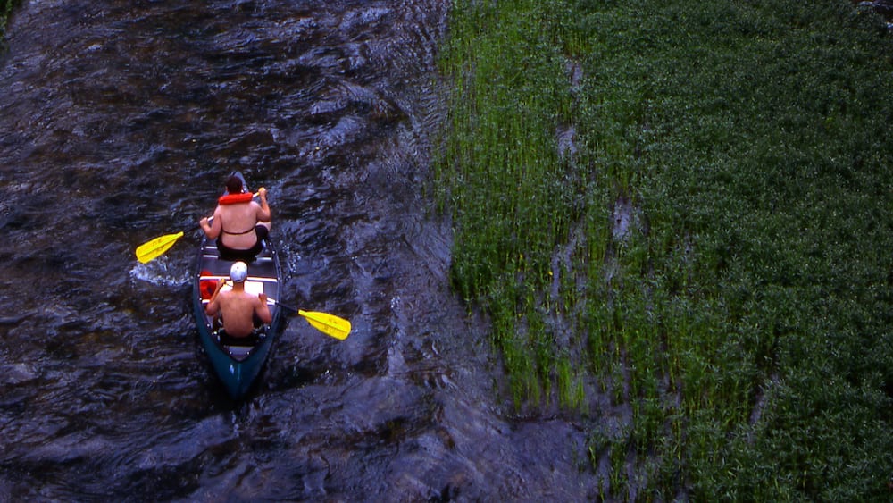 Une rivière avec un kayak et deux personnes qui pagayent.