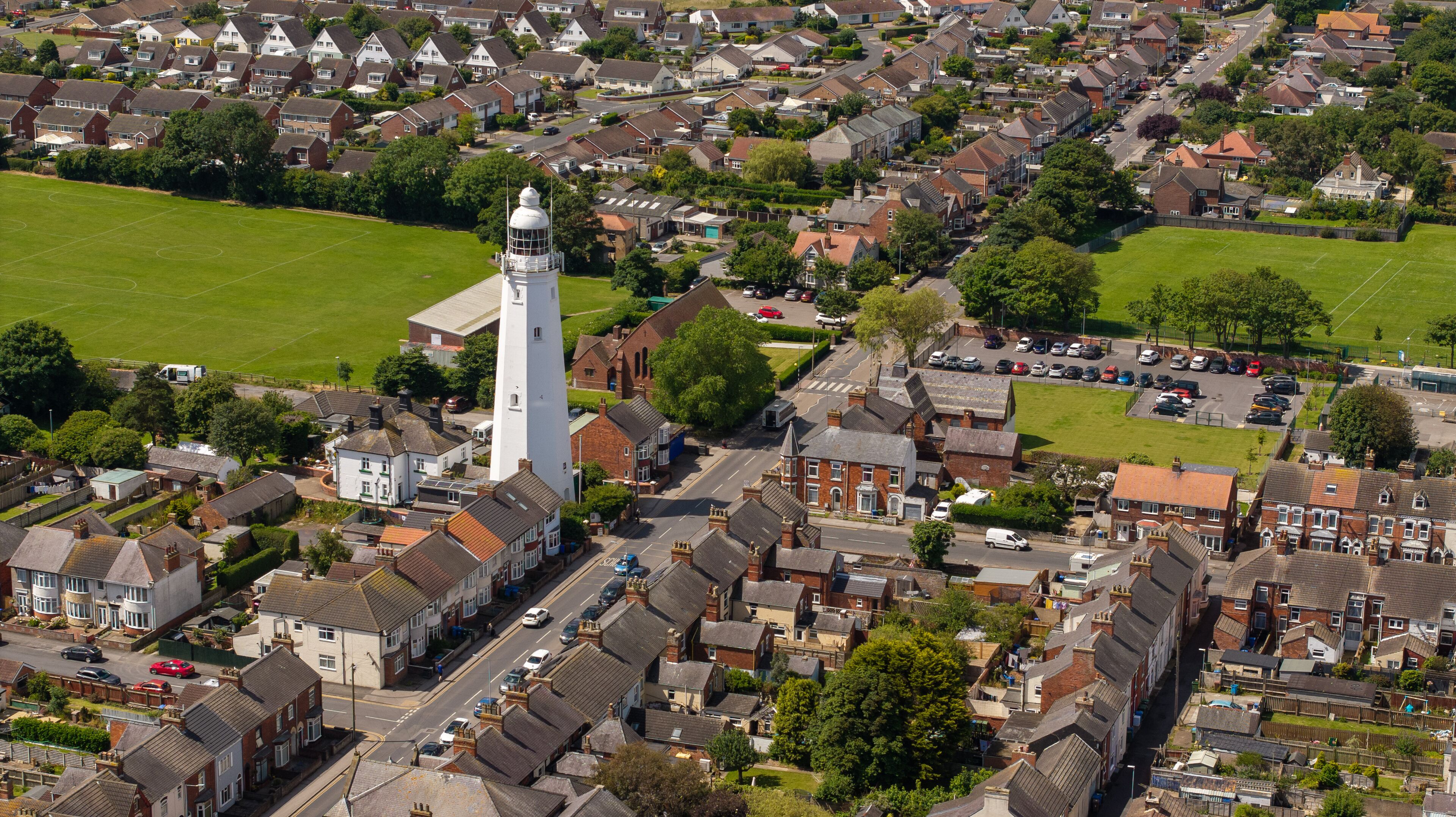 An aerial view of a residential area with houses, a prominent white tower, and a green field.