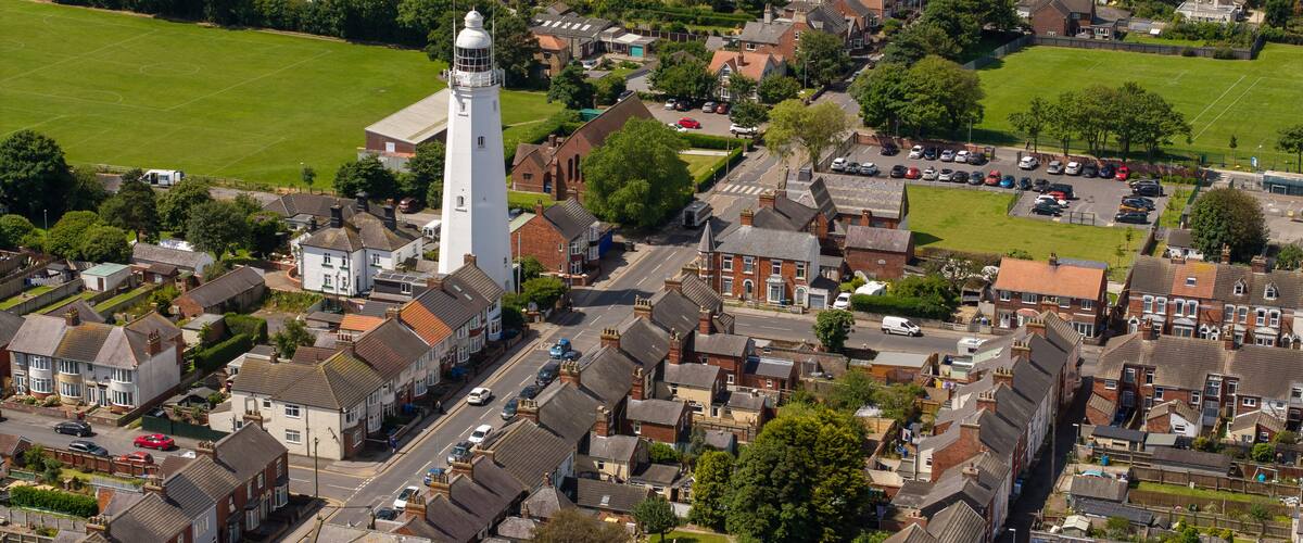 An aerial view of a residential area with houses, a prominent white tower, and a green field.