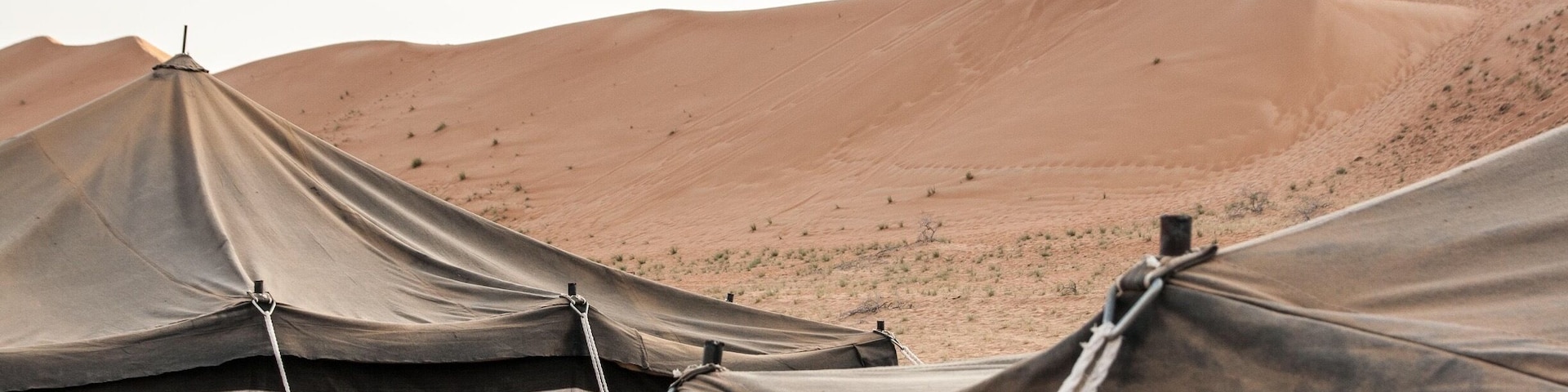 Paisaje desértico con tiendas de campaña y dunas de arena.