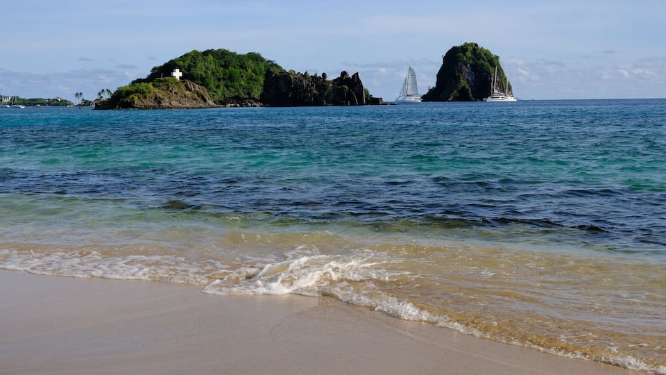 A beach with clear turquoise water, a sandy shore, and two small islands with rocky outcrops and greenery.