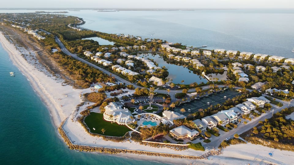 An aerial view of a coastal resort with a beach, water bodies, and a golf course.