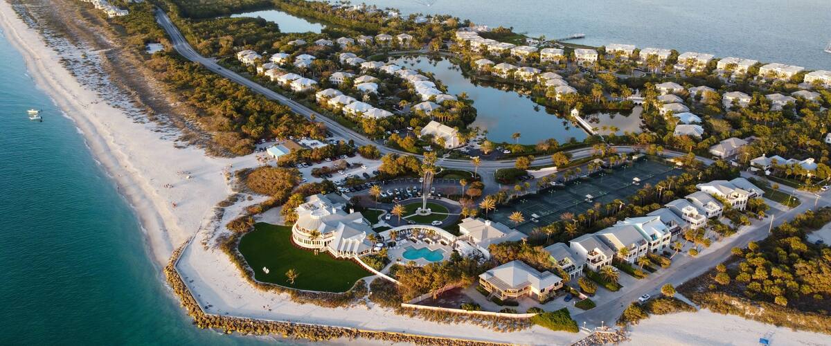 An aerial view of a coastal resort with a beach, water bodies, and a golf course.