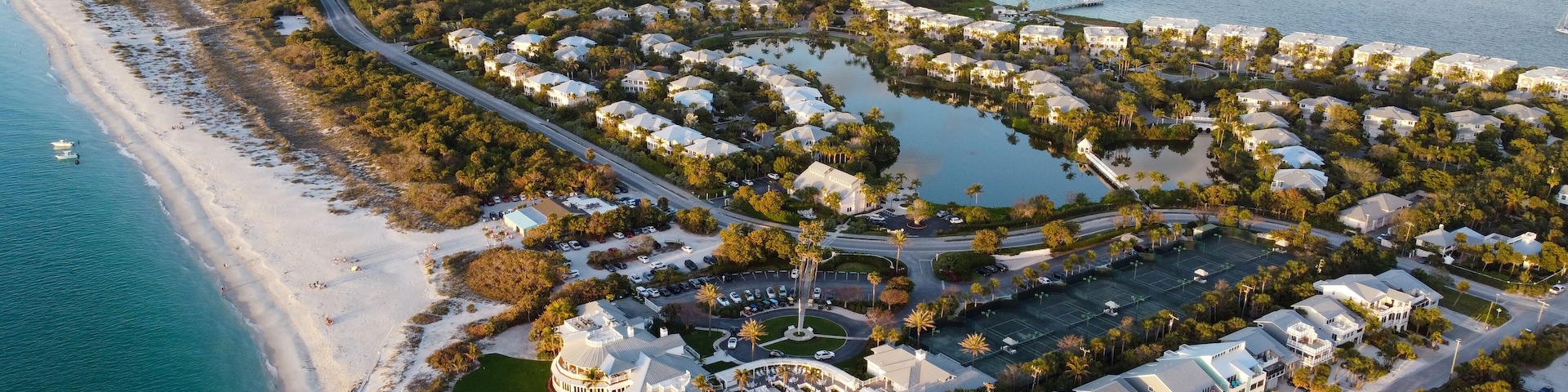An aerial view of a coastal resort with a beach, water bodies, and a golf course.