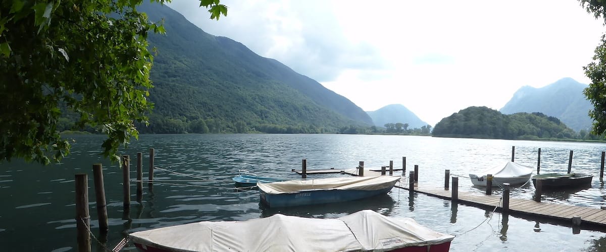 A calm lake with boats docked at a wooden pier, surrounded by lush green mountains.