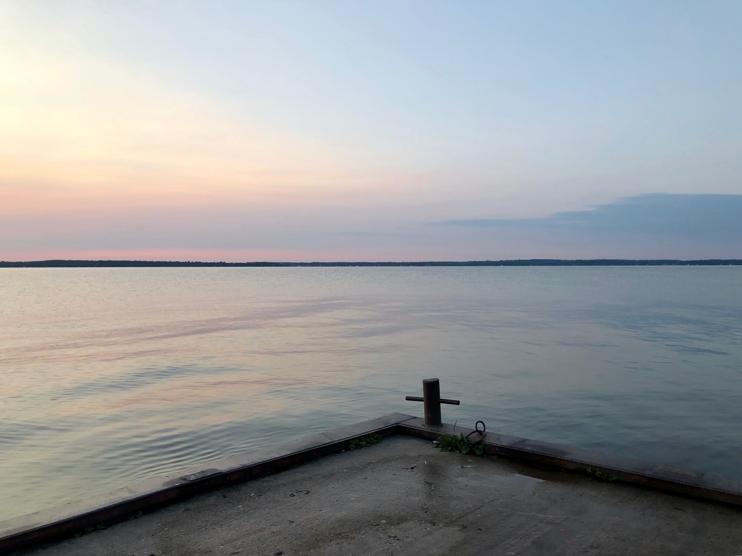A calm body of water with a concrete dock and a metal railing.