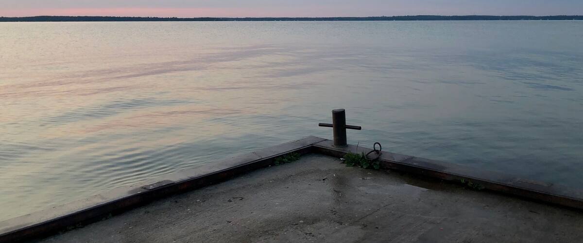 A calm body of water with a concrete dock and a metal railing.