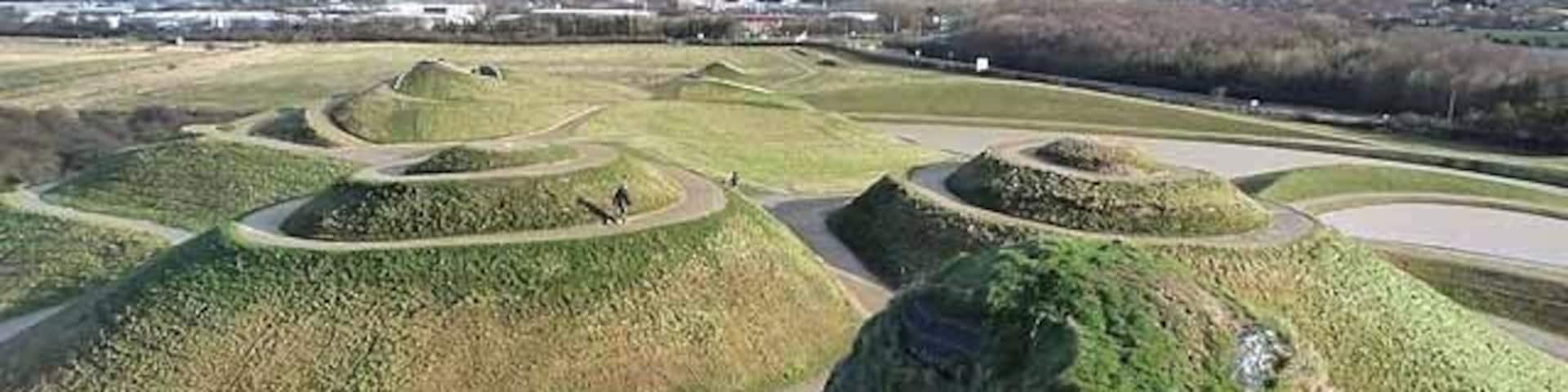 A series of mounds and a winding road in a grassy landscape.