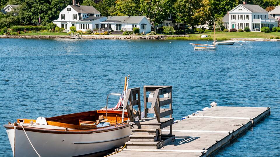 A wooden dock with a small boat tied to it, a wooden pier, and houses in the background.