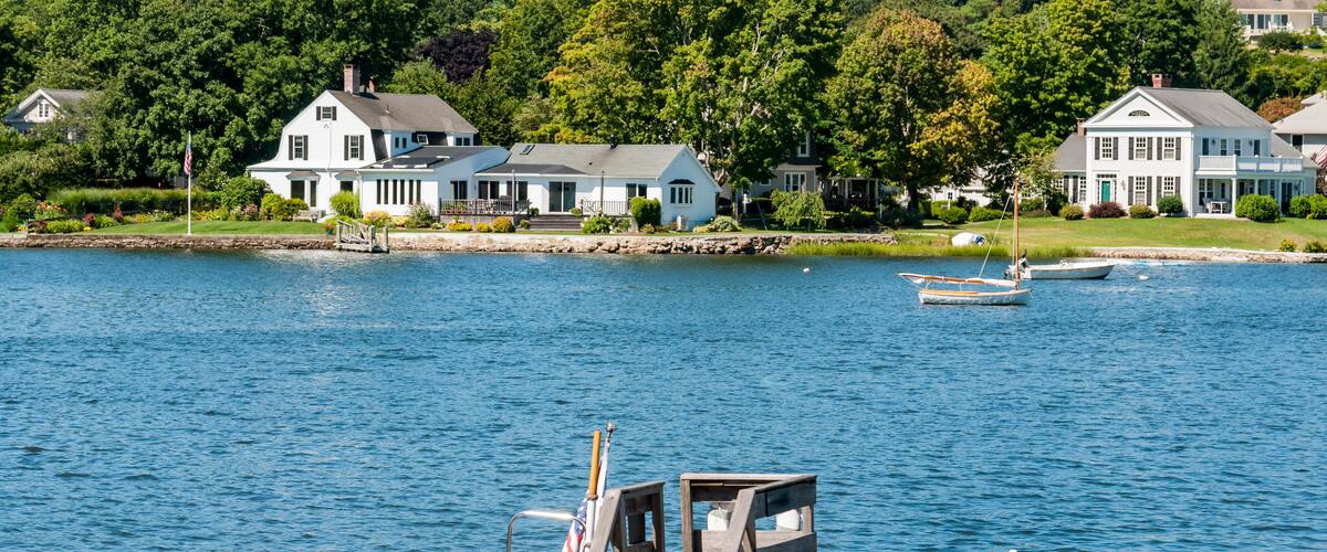 A wooden dock with a small boat tied to it, a wooden pier, and houses in the background.