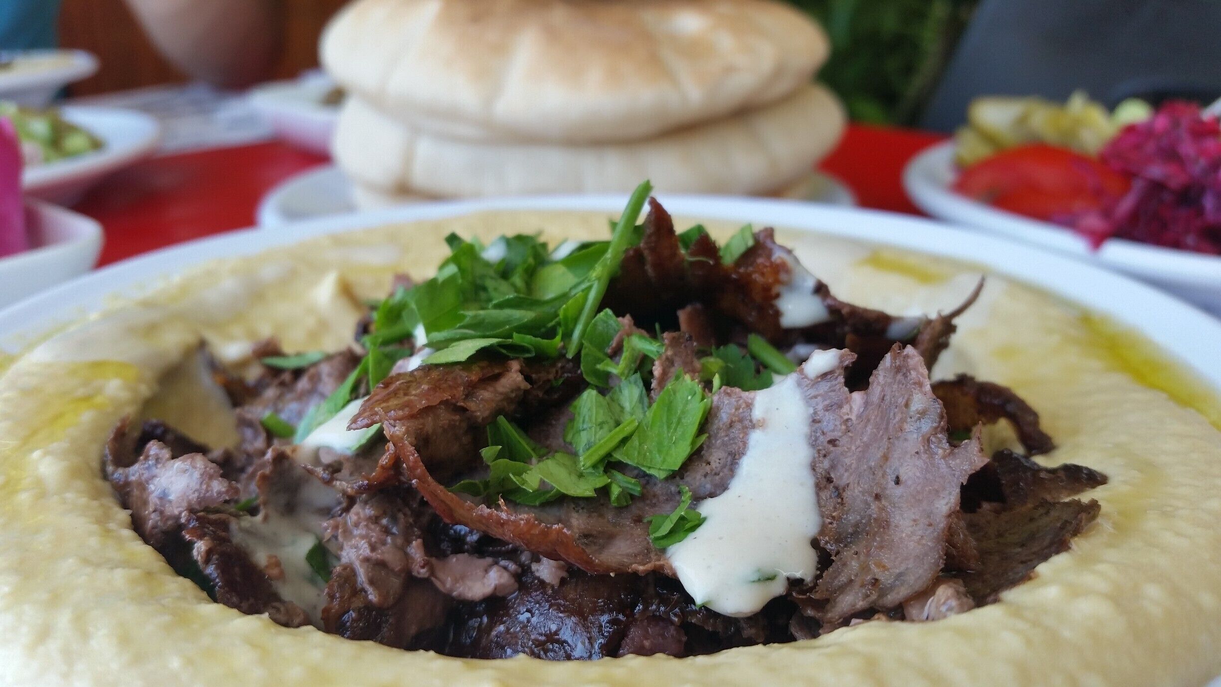 A dish of meat and hummus with a side of vegetables.