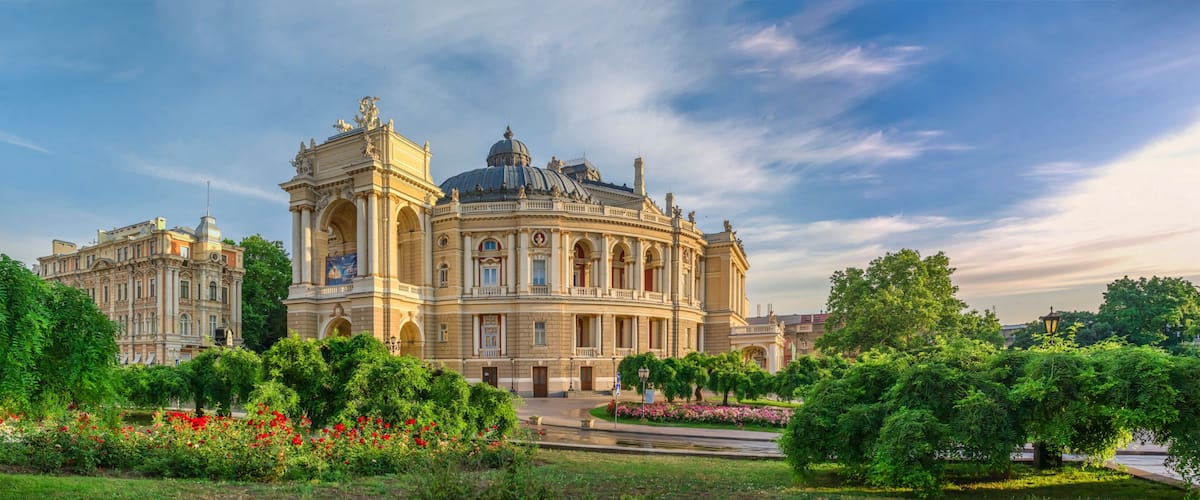 A grand historic building with a dome and classical architecture, surrounded by lush greenery and a well-maintained garden.