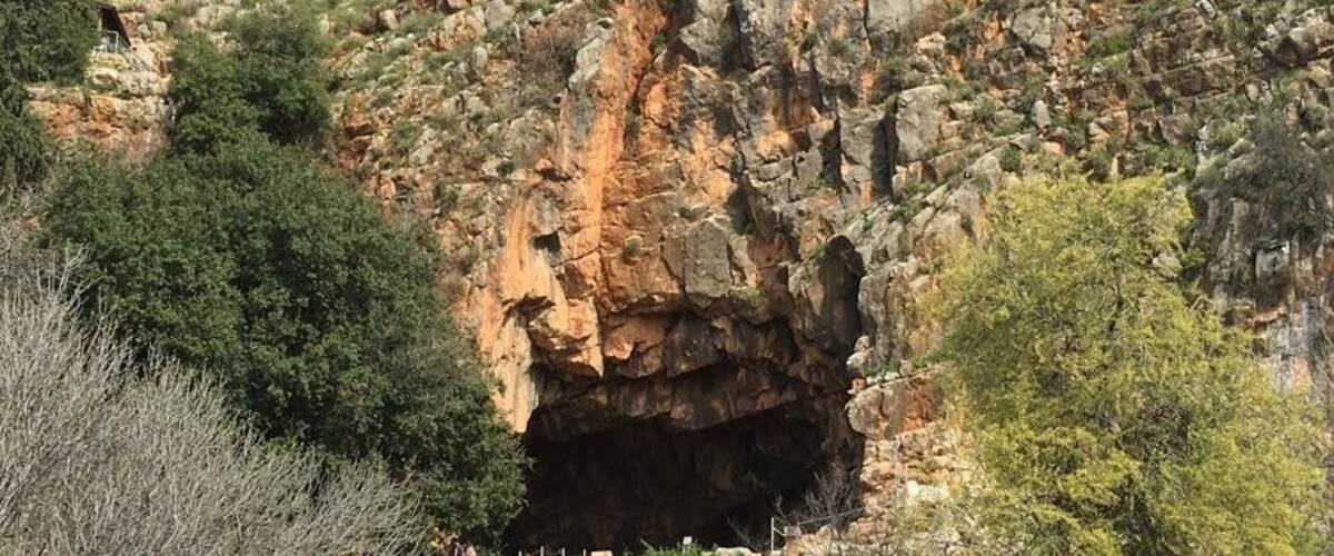 A rocky cliff with a cave entrance and a wooden structure on top.