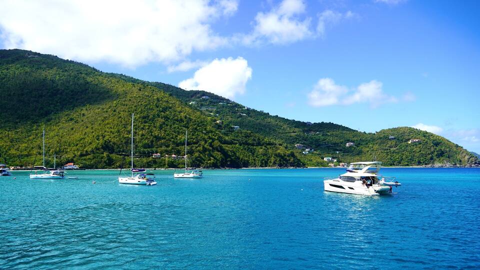 A turquoise sea with several sailboats anchored near a green, forested island.