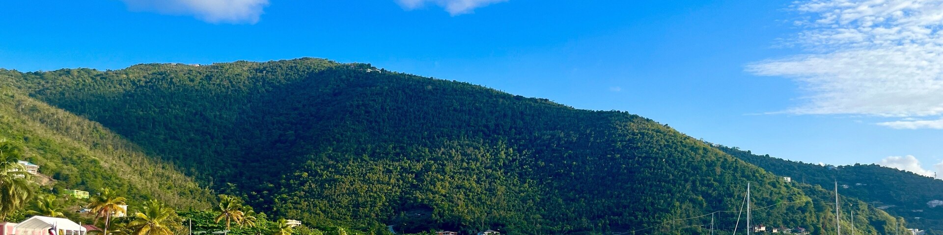 Uma praia com águas turquesa cristalinas, areal arenoso e uma colina arborizada ao fundo.
