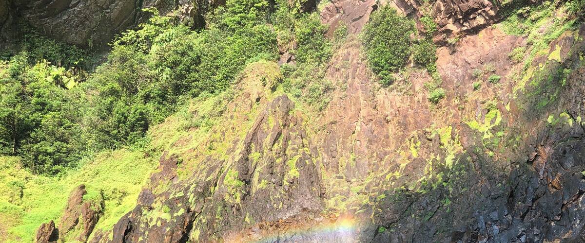 A rocky landscape with a waterfall and a rainbow.