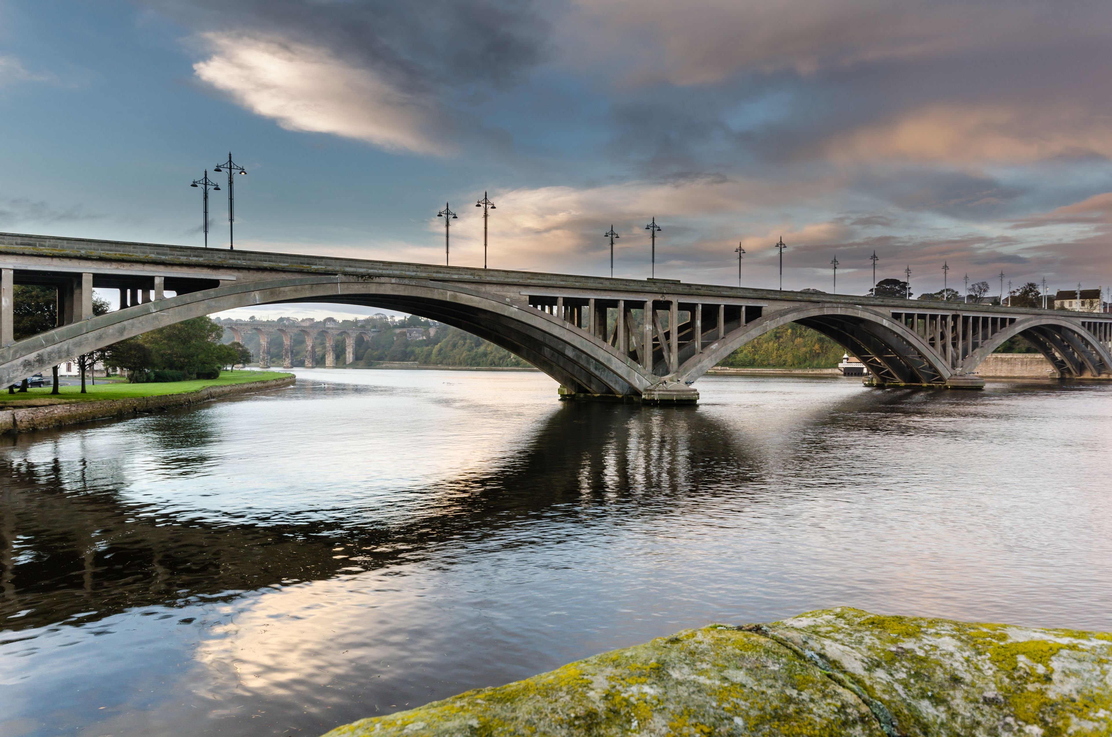 A stone bridge over a river with a cloudy sky.