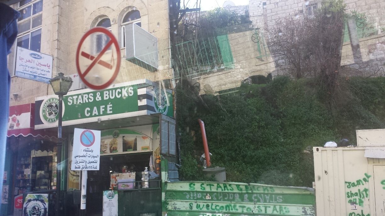 A Stars & Bucks café with a no smoking sign, a green awning, and a building with a stone facade.