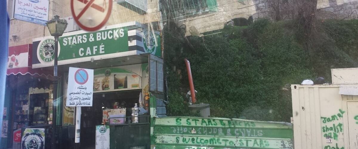 A Stars & Bucks café with a no smoking sign, a green awning, and a building with a stone facade.