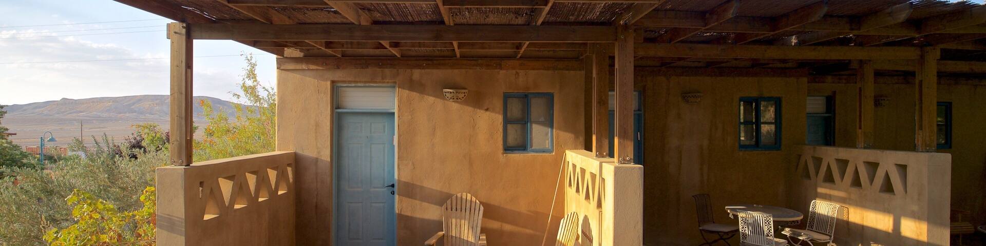 A rustic outdoor seating area with a wooden pergola, a door, and a table with chairs.