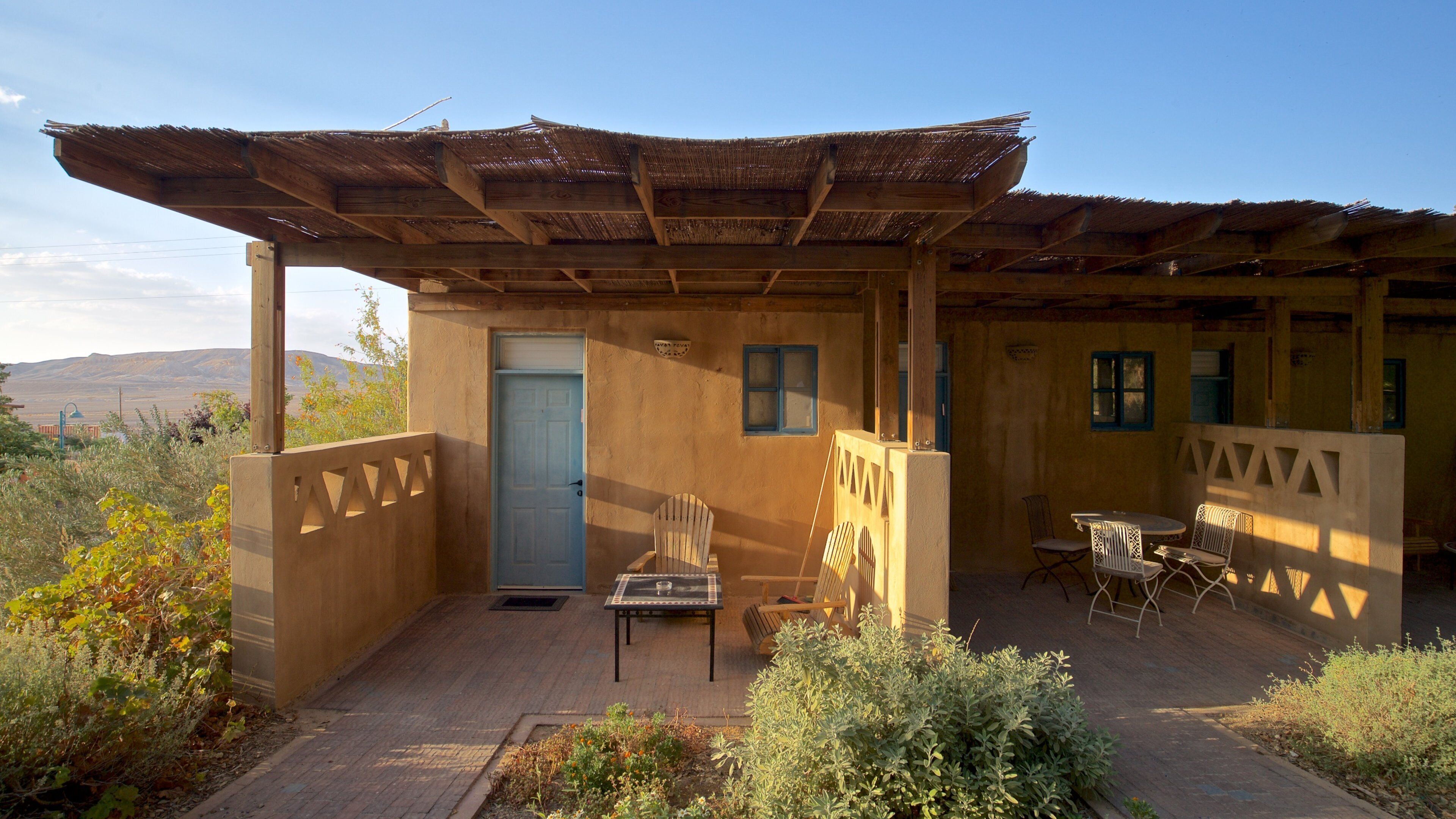 A rustic outdoor seating area with a wooden pergola, a door, and a table with chairs.
