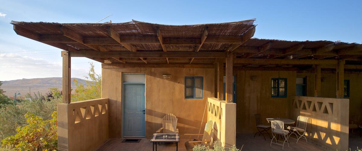 A rustic outdoor seating area with a wooden pergola, a door, and a table with chairs.