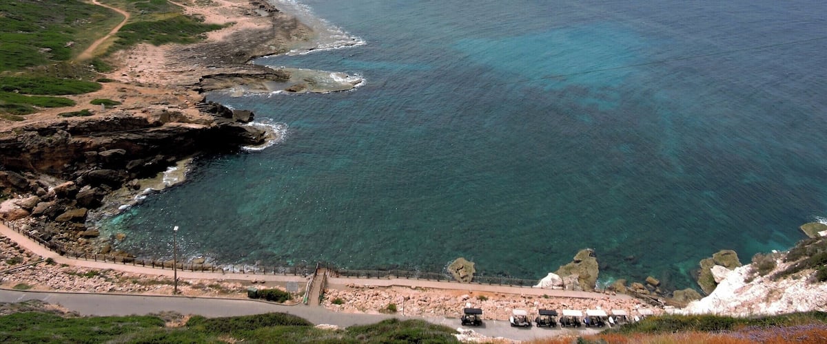 A coastal landscape with a clear view of the ocean, a winding road, and rocky cliffs.