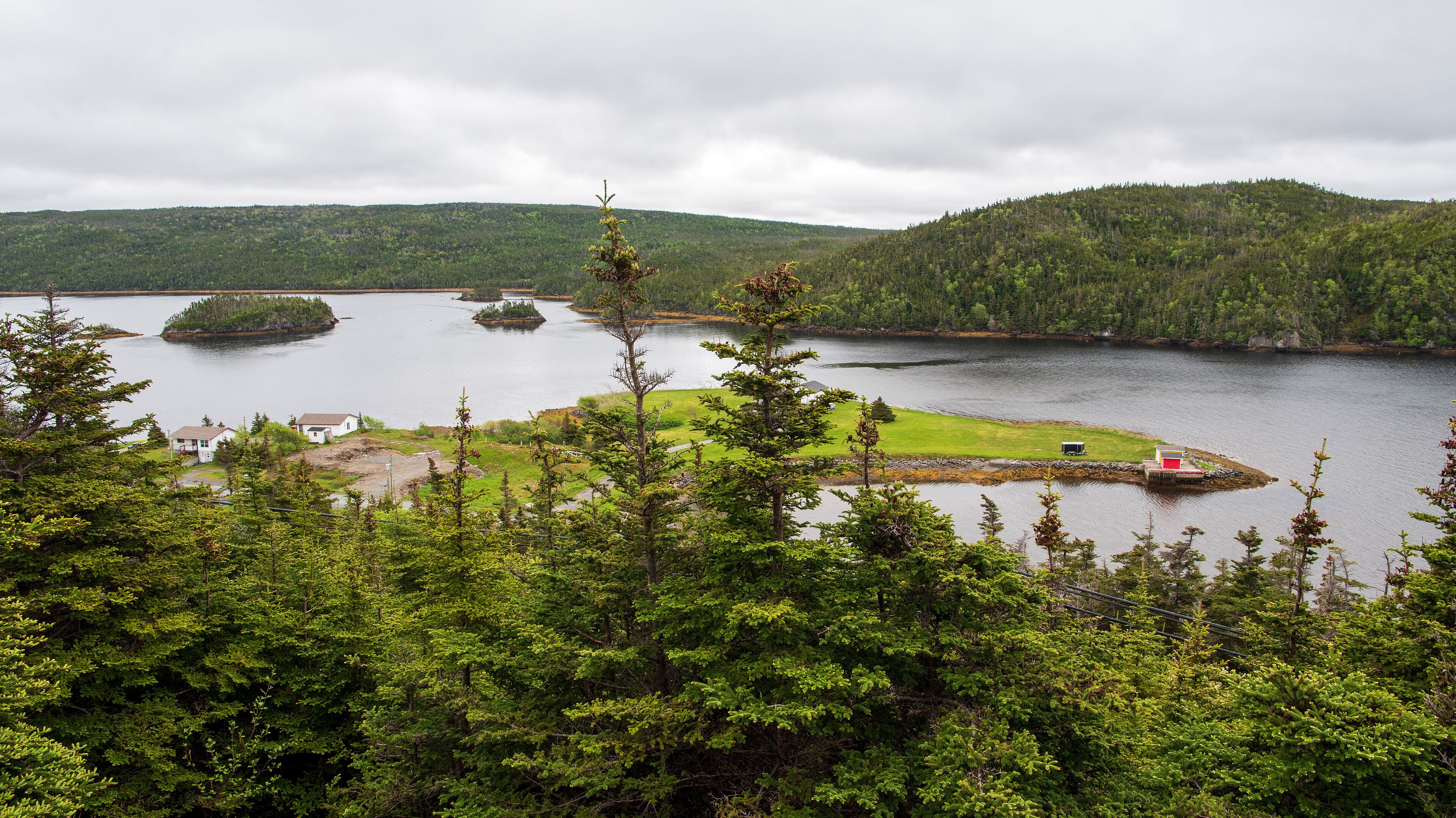 A lake surrounded by forested hills, a small island, and a white house with a red roof.