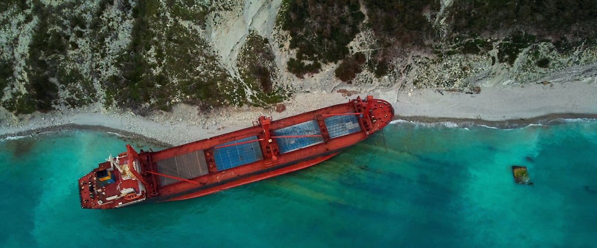 An abandoned ship stranded on a turquoise beach with white sand and sparse vegetation.