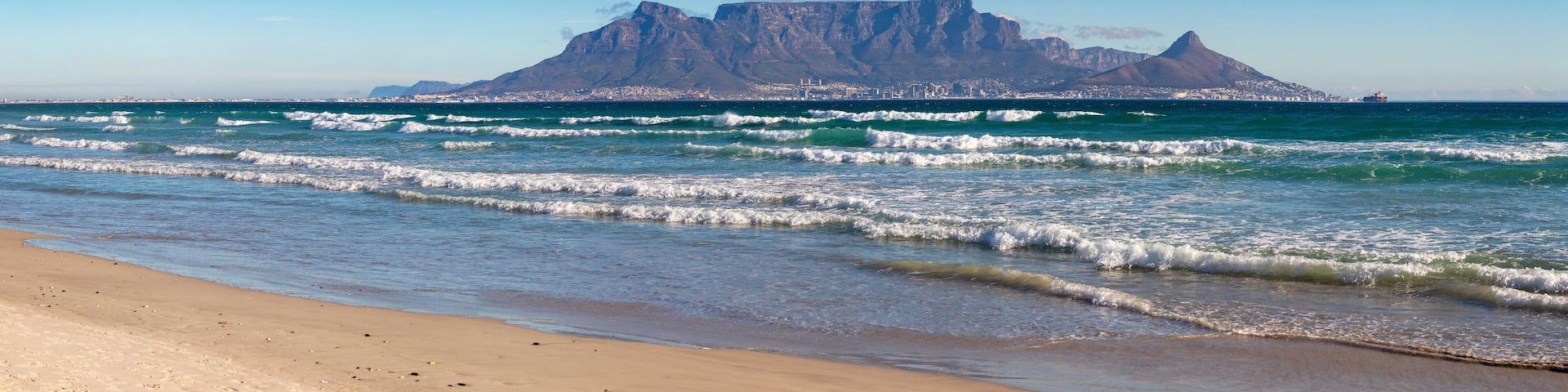 A beach with waves, a clear sky, and a mountain in the background.