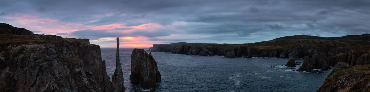 A coastal landscape with rocky cliffs and a sunset over the ocean.