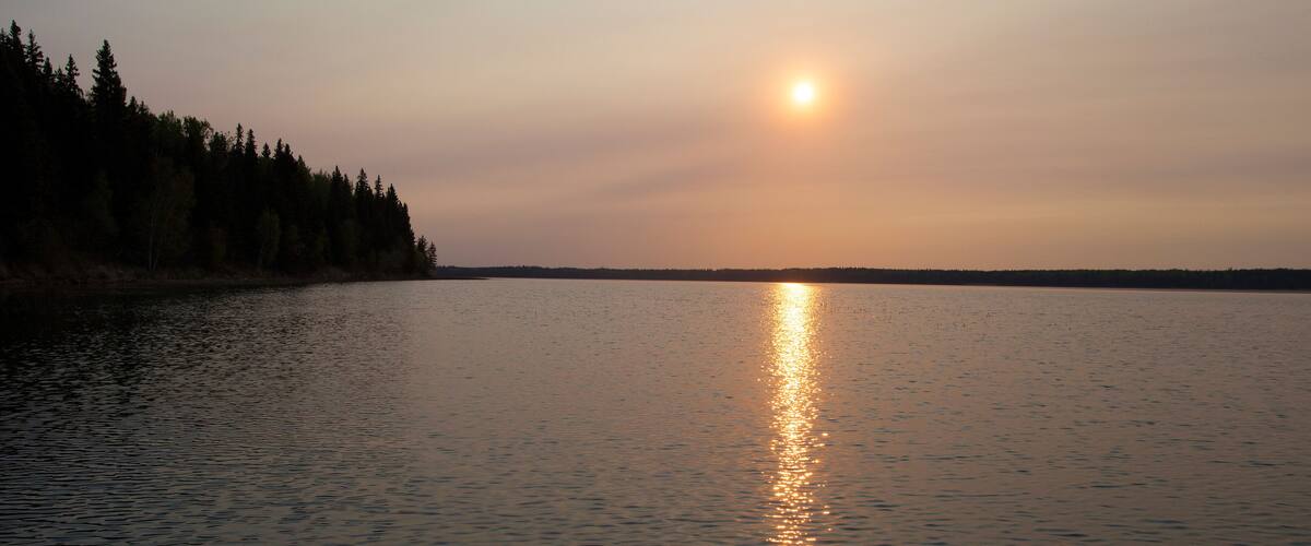 A calm lake at sunset with a forest on the left and a clear sky.