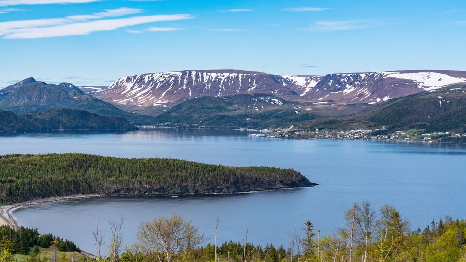 A lake surrounded by mountains with snow-capped peaks and a forested shoreline.