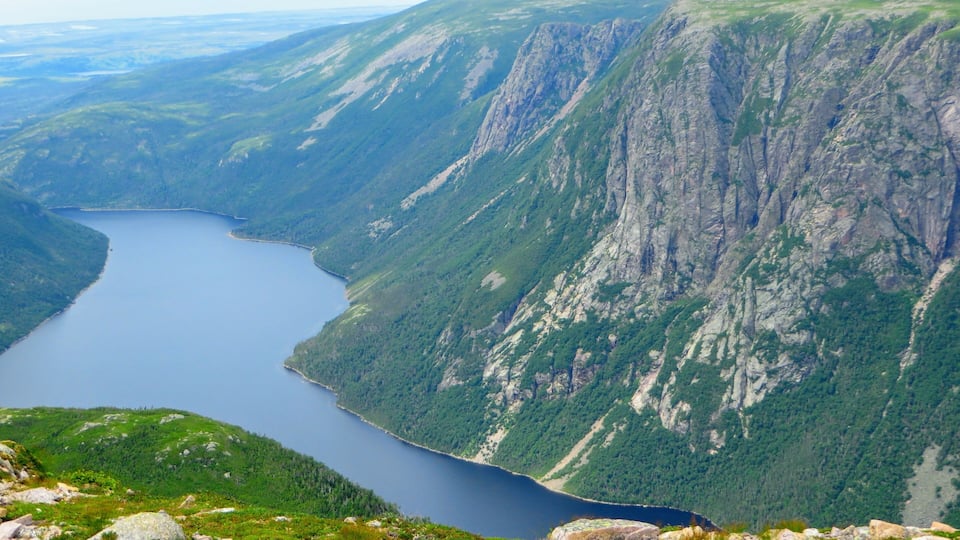 A mountainous landscape with a lake surrounded by steep cliffs and dense forests.