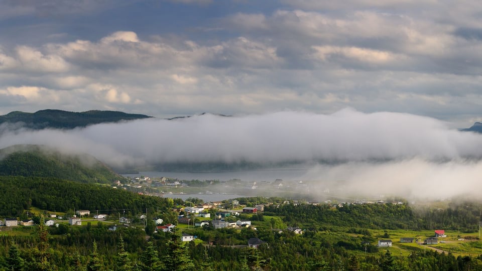 A coastal village surrounded by mountains and dense forests, with a lake and mist-covered peaks.