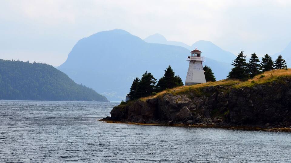 A lighthouse on a rocky outcrop with a forested hill in the background.