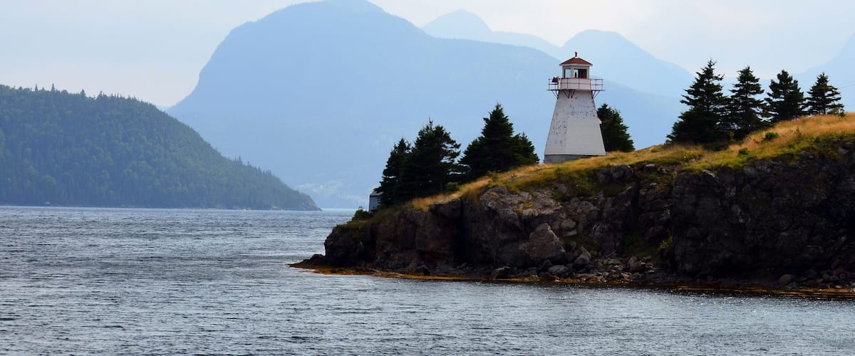 A lighthouse on a rocky outcrop with a forested hill in the background.