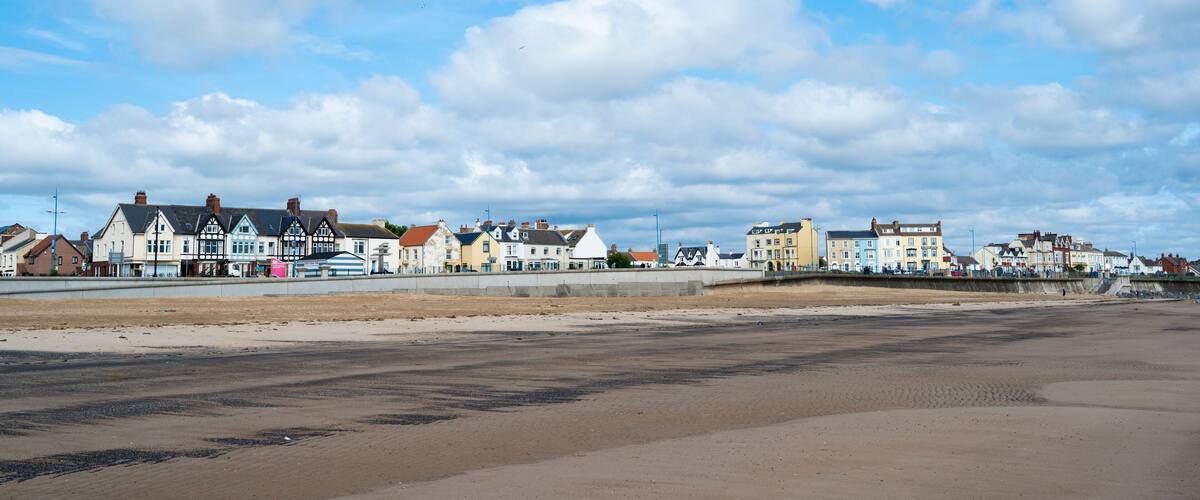 A coastal town with colorful buildings along the beach under a partly cloudy sky.