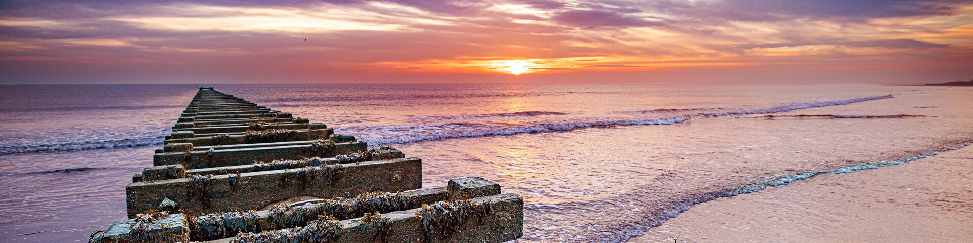 Un muelle de madera que se adentra en el océano al atardecer, con un cielo de colores.