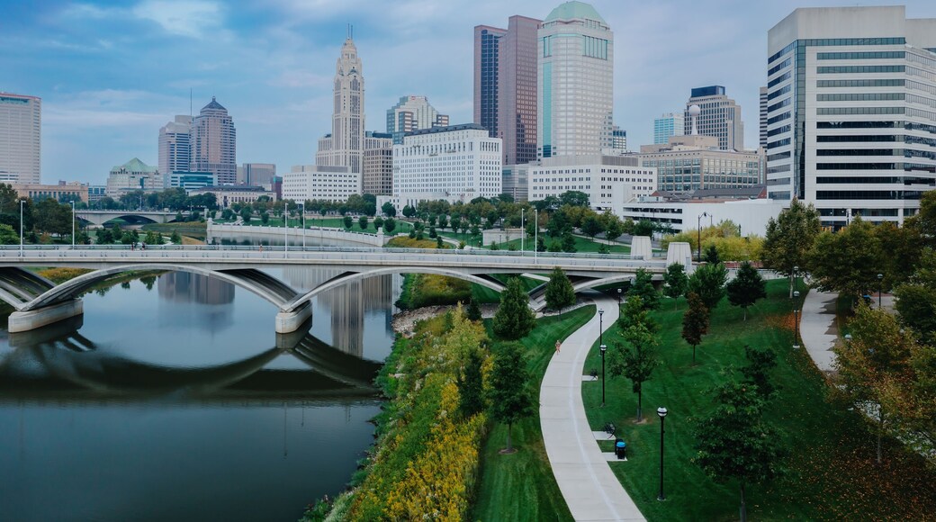 Runner on paved path, city skyline reflected in river, urban park. EAST BANK PARK, COLUMBUS, OHIO, UNITED STATES