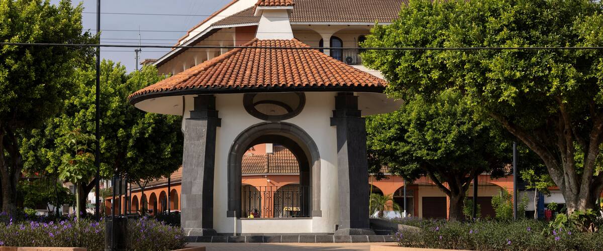 A courtyard with a central gazebo, surrounded by trees and a building with a tiled roof.