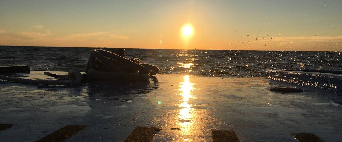 A sunset over the ocean with a boat and a buoy on the water.