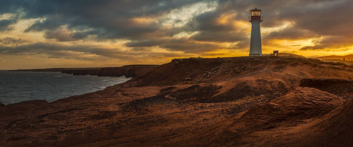 A lighthouse on a rocky cliff overlooking the sea during sunset.